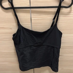 Svart linne från Lindex stl S - Svart linne från Lindex i ett glansigt material. Den har justerbara axelband. Mycket bra skick