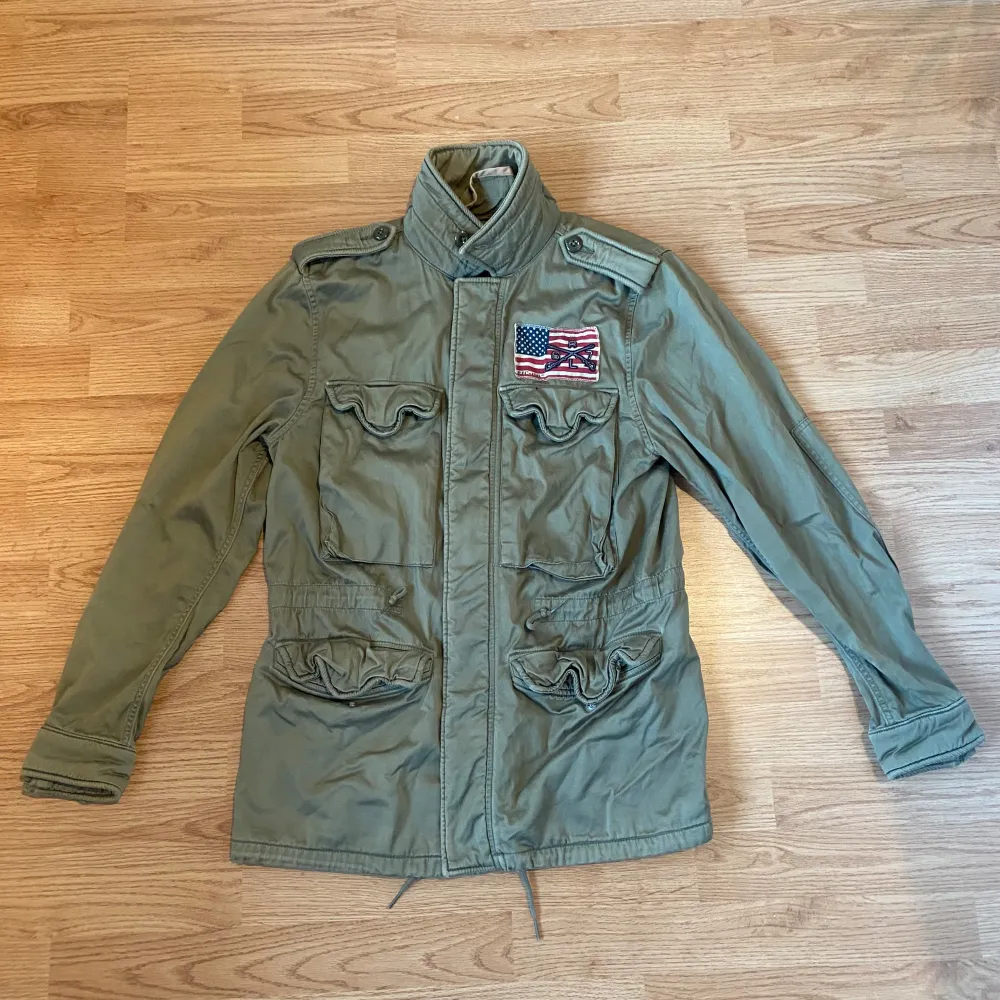 Säljer en grön field jacket från Polo Jeans Company, Ralph Lauren. Den har en cool amerikansk flagga med broderade detaljer på bröstet. Storlek S. Jackan är i bra skick och perfekt nu till hösten. Tveka inte att kontakta vid minsta lilla fundering.. Jackor.