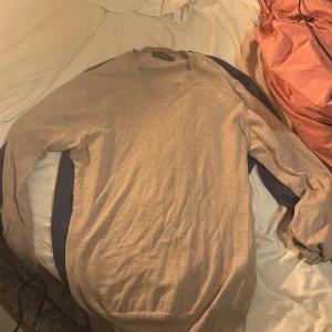 Beige tröja från Oscar Jacobson - Säljer en stilren beige tröja från Oscar Jacobson. Perfekt för både vardag och lite finare tillfällen. Tröjan har en klassisk rund hals och långa ärmar. Den är i mycket bra skick och passar perfekt till höst- och vårgarderoben.