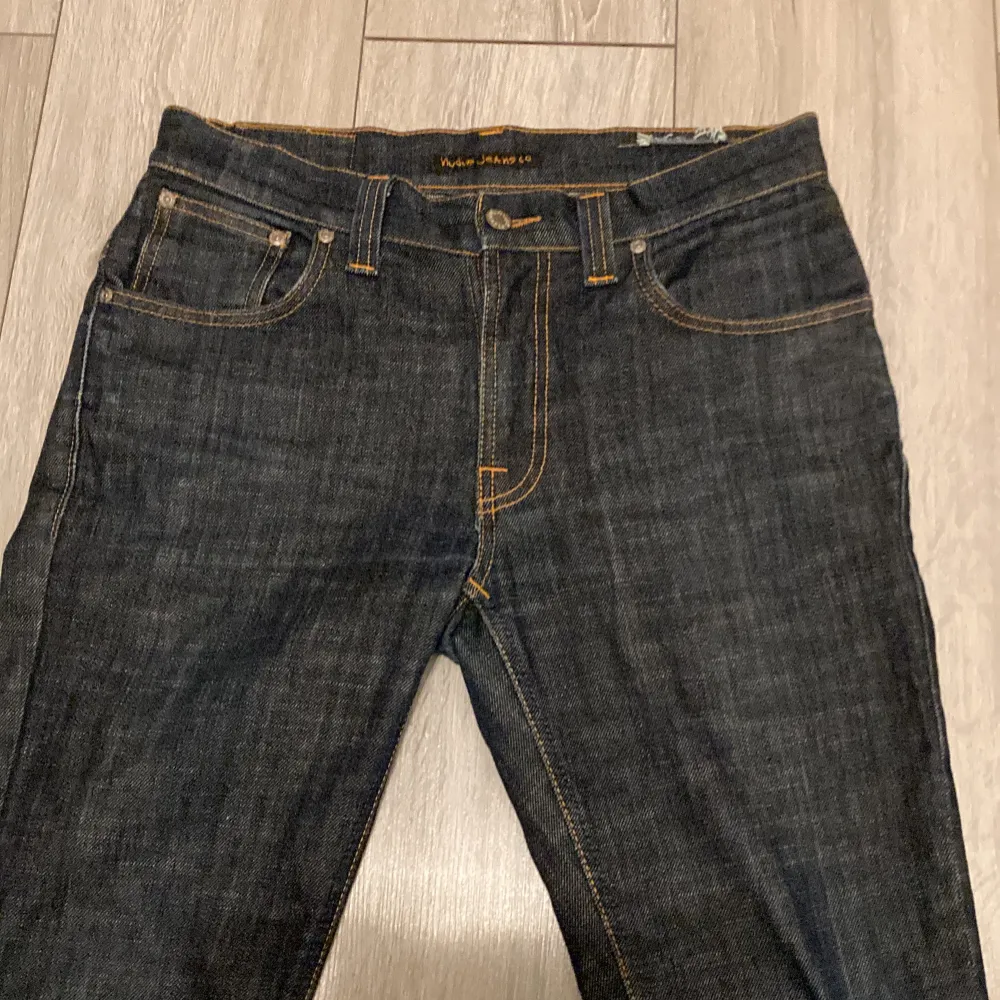 Säljer ett par snygga mörkblå jeans från Nudie Jeans i storlek W31 L32. De har en klassisk femficksdesign med orange sömmar och en bekväm passform. Perfekta inför vintern och är väldigt sköna och varma. Jeans & Byxor.