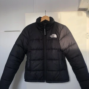 Svart dunjacka från The North Face - Säljer en snygg och varm svart dunjacka från the north face, tryck fram och bak, inga anmärkningar, har en tightare modell men är ändå varm och passar till både vår, höst och vinter:)