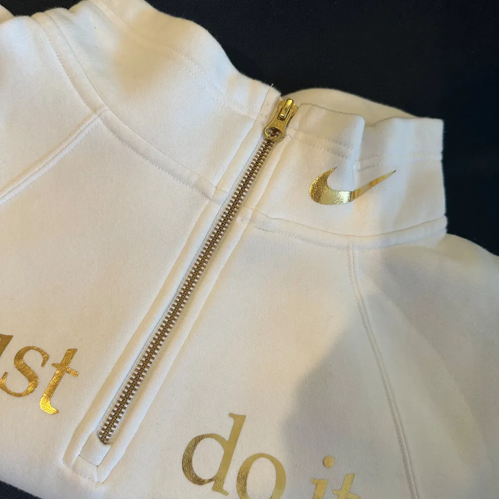 Säljer en snygg vit tjockare tröja med hög krage från Nike med det ikoniska 'Just do it.' trycket i guld på framsidan. Den har en dragkedja vid halsen och Nike-loggan i guld. Perfekt för en sportig och stilren look. Materialet är en blandning av bomull och polyester, vilket gör den både bekväm och hållbar. Passar S/M . Tröjor & Koftor.