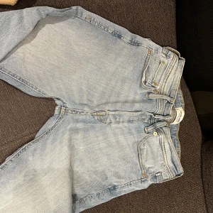 Ljusblå jeansbyxor - Säljer ett par ljusblå jeans i bra skick. De har en klassisk femficksdesign och är tillverkade i denim. Perfekta för vardagsbruk och kan matchas med nästan vad som helst. Passformen verkar vara straight och de har en knappgylf.