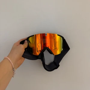 Skidglasögon från Salomon - Säljer ett par coola skidglasögon från Salomon i svart med spegelglas i rött/orange/gult. De kommer med förvaringspåsen och originalkartong. Glasögonen är i superfint skick, använd en gång! Köpt förra året