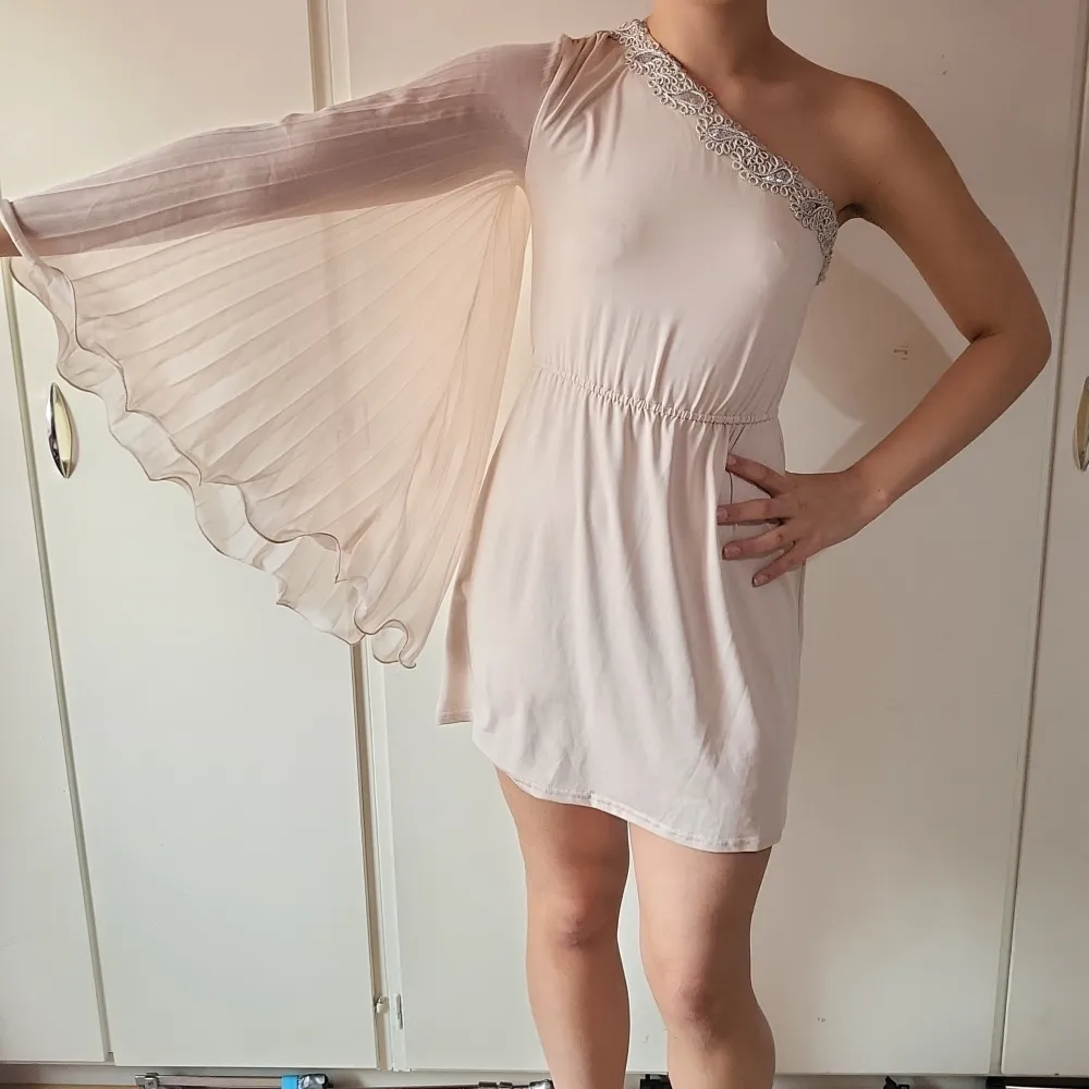 Beige klänning med detaljer. Detaljerna går hela vägen runt klänningen. Likadan framsida som baksida. Arm i chiffong. Nyskick/oanvänd (prislapp sitter kvar) . Mekot.