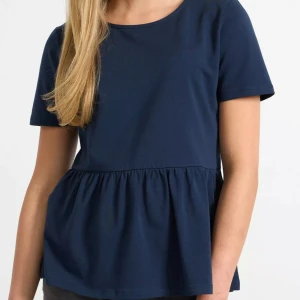 Mörkblå topp med volangdetalj - Säljer en söt mörkblå topp med korta ärmar och volangdetalj i nederkant. Perfekt för både vardag och festliga tillfällen. Toppen är i ett mjukt och bekvämt material som känns skönt mot huden.