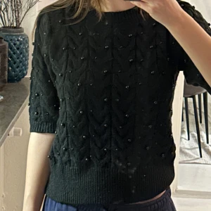 Svart stickad topp med pärlor från Zara - Stickad T-shirt från Zara i strl M. Tröjan har ett ”flätat” mönster och har insydda svarta runda pärlor. Använd ca 2 ggr och är i mycket gott skick. Pris kan diskuteras