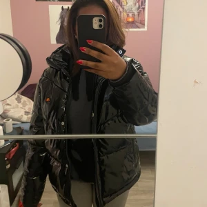 Svart glansig pufferjacka från Ellesse - Säljer en svart glansig pufferjacka från Ellesse i storlek EU 36. Jackan har en hög krage och huva, perfekt för kyliga dagar. Den har en dragkedja och tryckknappar framtill. Superstylish och håller dig varm hela vintern! Ordinarie pris 1260 🖤