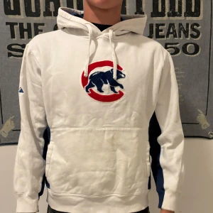 Vit hoodie med blå detaljer och logga - Säljer en vit hoodie med en cool logga på framsidan. Den har blå detaljer längs sidorna och ärmarna. Perfekt för en avslappnad stil och håller dig varm under kyliga dagar. (Den har en klassisk passform och är i bra skick men har lite fläckar på fickan) köpt för 500kr på broadway & sons vid domkyrkan.