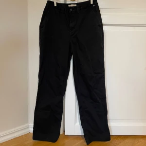 Svarta Vans byxor - Säljer ett par klassiska svarta byxor i mycket bra skick. De har en normal passform och är perfekta för både formella och semi-formella tillfällen. Byxorna har knappar och dragkedja. 