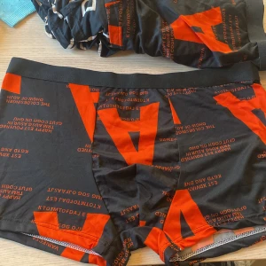 Svarta boxershorts med mönster - Helt Nya!! (6st Totalt) Säljer tre par svarta boxershorts med superskönt material med olika mönster. Ett par har stora röda bokstäver, ett annat har ett guldigt och vitt mönster, och det sista paret har vita konturer. Perfekta för vardagsbruk och superbekväma! Storleken står XL men är mer som Medium/Large!