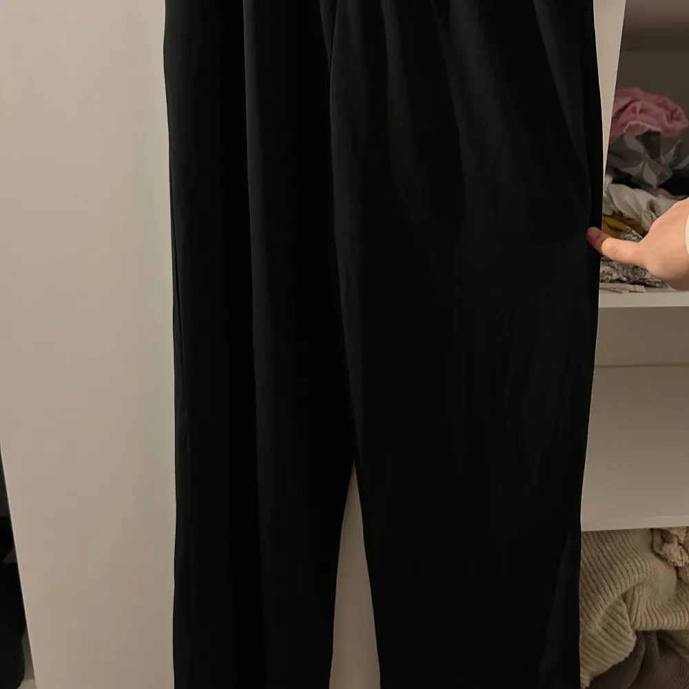 Elegant svart jumpsuit med v-ringning och vackra spetsdetaljer längs framsidan. Klänningen har långa ärmar och en figursmickrande passform, perfekt för festliga tillfällen. Materialet är mjukt och följsamt, vilket ger en bekväm känsla hela kvällen.. Övrigt.