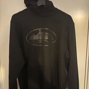  hoodie från cortiez triple black - Säljer en svart hoodie från cortiez i storlek medium det är en skön tröja  med ett coolt tryck på framsidan. Perfekt för höst och vinter med sin mysiga och bekväma passform. Den har en klassisk känguruficka och en skön huva. Passar både till vardags och chillkvällar. 🖤