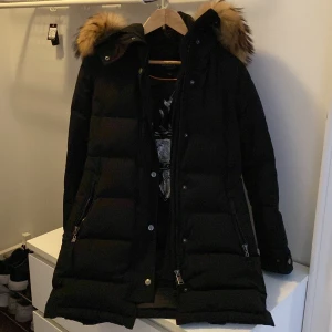 Svart dunjacka från Hollies - Säljer en svart dunjacka från Hollies i storlek 34. Jackan har en mysig pälskantad huva och stängs med både dragkedja och knappar. Perfekt för kalla vinterdagar! Observera att det finns en liten reva på insidan. 🖤Nypris 4995kr använd bara en vinter, passade inte längre till nästa vinter, revan är fråninsidan och syns inte! Passar perfekt även till storlek 36/S då jackan är stor i storlek. Köptes från Miinto.