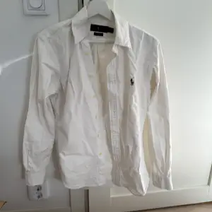 Säljer en klassisk vit skjorta från Ralph Lauren i slim fit. Skjortan är i stretchigt oxford-tyg och har långa ärmar. Den har knappar framtill och en broderad logga på bröstet. Perfekt för både vardag och fest! 🕺