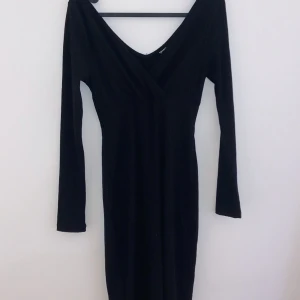 Svart långärmad klänning - Elegant svart klänning med lång ärm och v-ringad design. Perfekt för höst- och vinterfester. Den har en tight passform som framhäver figuren och är gjord i ett mjukt och bekvämt material.