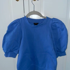 Blå tröja från Lindex - Säljer en superfin blå tröja från Lindex i storlek XS pga att den inte kommer till användning. Den har puffiga kortärmar som ger en söt och trendig look. Perfekt för både vardag och fest! 💙
