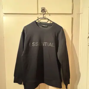 Säljer en stilren svart sweatshirt från Essentials. Den har en enkel design med texten 'ESSENTIAL' tryckt på framsidan. Tröjan är långärmad och perfekt för både vardag och avslappnade tillfällen. Passar bra till jeans eller träningsbyxor.