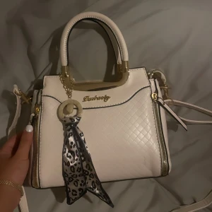 Vit handväska med leoparddetalj - Säljer en snygg vit handväska med quiltad design och leopardmönstrad scarfdetalj. Väskan har guldfärgade detaljer och en praktisk dragkedja. Perfekt för både vardag och fest. Väskan är helt ny och har aldrig kommit till användning💓