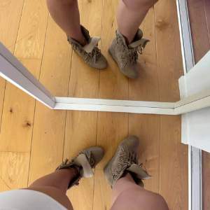 Säljer ett par snygga beige mockaboots med fransar. De har snörning framtill och är perfekta för höst och vår. Bootsens fransar ger en bohemisk touch och de är i mycket bra skick. Perfekta för att ge din outfit lite extra stil!