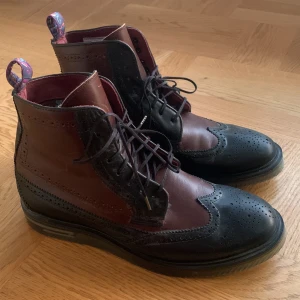 Svart och vinröd brogue boots - Snygga brogue boots från Ted Baker i svart och vinrött skinn. De har klassiska broguemönster och snörning framtill. Perfekta för höst och vinter med en stilren look. Skorna är i mycket bra skick. Passar både till vardags och fest! Stl UK8 som borde vara stl 42
