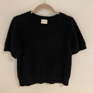 Svart tröja från Vila - Mysig svart tröja från Vila i ett fluffigt material. Perfekt för en stilren look, med korta ärmar och rund hals. Passar bra till både vardag och fest. 🖤