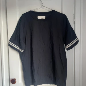 Svart t-shirt från Our Legacy - Säljer en stilren svart t-shirt från Our Legacy i storlek m-l. Den har korta ärmar med vita ränder som ger en stilren touch. Perfekt för både vardag och fest. Materialet känns mjukt och bekvämt. Passar både dam och herr!