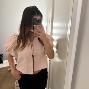Rosa kortärmad topp med knyt - Säljer en söt rosa topp med korta puffärmar och knyt framtill. Perfekt för sommardagar eller en avslappnad fest. Toppen är croppad och har en luftig passform som ger en skön känsla. Passar bra till både jeans, kjol eller kostymbyxor! Denna topp är aldrig använd och har prislapp kvar!