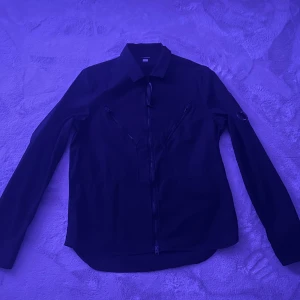 Svart jacka från C.P. Company - Säljer en stilren svart jacka från C.P. Company. Den har en dragkedja framtill och coola detaljer som dragkedjor på bröstet. Perfekt för höst och vår. Jackan har en klassisk krage och är långärmad. Passar både till vardags och lite finare tillfällen. 