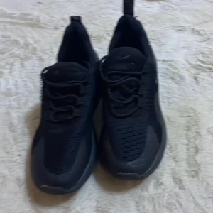 Svarta Nike sneakers - Säljer ett par svarta Nike sneakers i mycket bra skick. De har en stilren design med snörning och är perfekta för både träning och vardagsbruk. Skorna är tillverkade i syntetmaterial och har en bekväm passform. Sulan är robust och ger bra grepp.