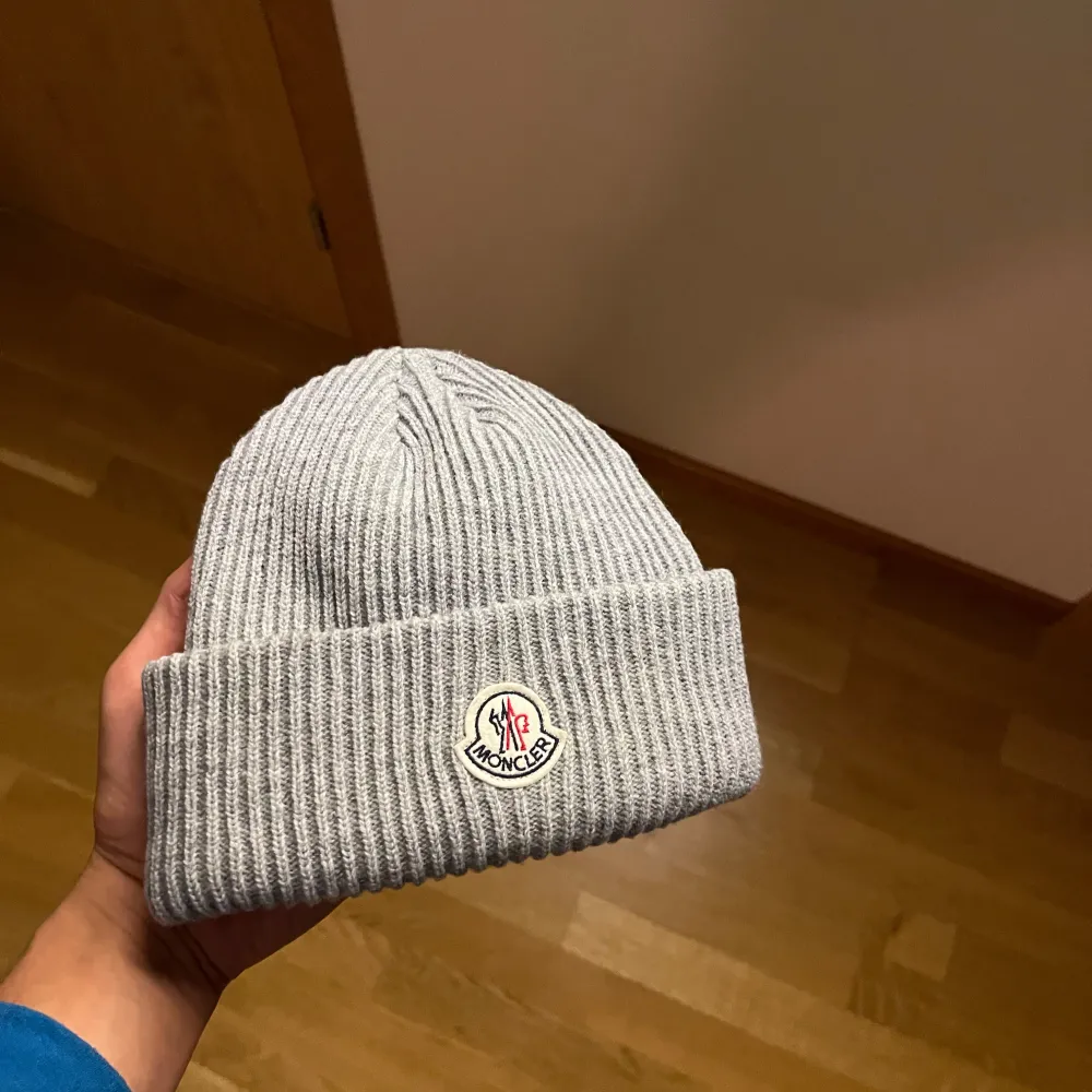 Säljer en snygg grå ribbad mössa från Moncler. Den är perfekt för kyliga dagar och har en stilren design med Monclers logga framtill. Mössan är i mycket bra skick och passar perfekt till vintern.. Accessoarer.