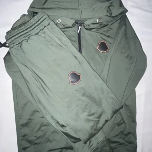 Grön tracksuit från Moncler - Säljer en snygg grön tracksuit från Moncler i mycket bra skick. Koftan har en dragkedja framtill och en huva för extra skydd. Den är långärmad och har Monclers logga både på bröstet och stort på ryggen. Perfekt för höst och vår! Lite dåligt vid dragkedjan d e drf den e billig 