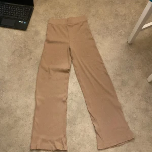 Beige ribbade byxor - Säljer ett par snygga beige ribbade byxor i storlek XS. De har en loose passform och är perfekta för både vardag och avslappnade tillfällen. Byxorna är högmidjade och superbekväma att ha på sig. Perfekta för höst och vår!