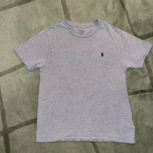 Grå t-shirt från Polo Ralph Lauren - Hej! Säljer en klassisk grå t-shirt från Polo Ralph Lauren i barn-storlek M(150cm, 10-12 år) . Säljer på grund av att jag har växt ur den. Den har en liten blå logga broderad på bröstet och är i bomull. Perfekt för en avslappnad stil och passar till det mesta. Skön och enkel att matcha! Köpt på nacka forum på kidsbarndstore ny för 400kr😁
