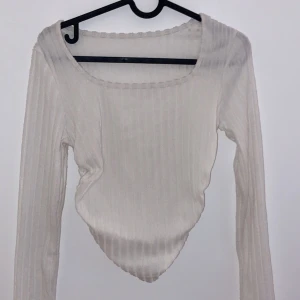 Vit ribbad långärmad topp - Säljer en stilren vit ribbad topp med långärmade ärmar. Den har en unik asymmetrisk nederkant som ger en cool look. Perfekt för både vardag och fest! 🖤