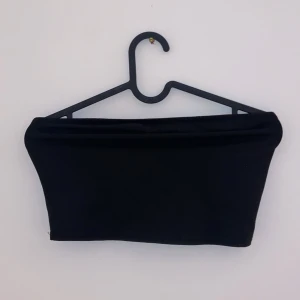 Svart tubtopp - Snygg och enkel svart tubtopp perfekt för sommaren. Den är ärmlös och har en tight passform som sitter bra på kroppen. Perfekt att matcha med ett par jeans eller en kjol för en stilren look.