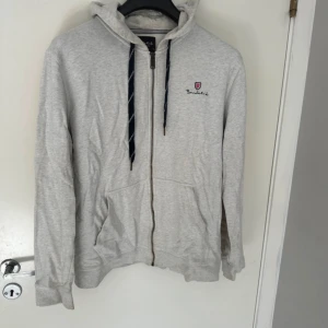 Grå hoodie från Bondelid - Säljer en snygg och bekväm grå hoodie från Bondelid. Den har en dragkedja framtill och justerbara snören i huvan. Perfekt för en avslappnad stil och passar till alla årstider. Den är i bra skick och redo för nya äventyr!