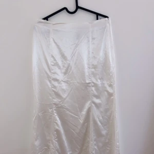 Vit långkjol i satin - Säljer en elegant vit långkjol i satin. Perfekt för festliga tillfällen eller en stilren vardagslook. Kjolen har en slät yta och ett vackert fall som ger en lyxig känsla. Passar bra till både sommar och vår. Ett måste i garderoben för den som älskar klassiska plagg!