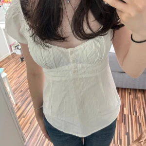 Vit blus från Brandy Melville - Säljer en söt vit blus från Brandy Melville. Den har korta puffärmar och knappar framtill. Perfekt för sommardagar eller en avslappnad vårlook. Blusen är i ett lätt och bekvämt material.