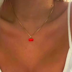 halsband med röd berlock - Snyggt halsband med en liten röd berlock som ser ut som ett körsbär. Perfekt för att lägga till en färgklick till din outfit. Halsbandet är enkelt och elegant, vilket gör det lätt att matcha med andra smycken. Passar både till vardags och fest!