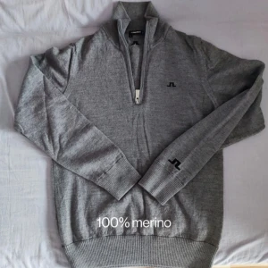 Grå merinoulltröja från J.Lindeberg - Säljer en stilren grå tröja i 100% merinoull från J.Lindeberg. Den har en praktisk dragkedja framtill och ribbade muddar för extra komfort. Perfekt för kyliga dagar och passar både till vardags och lite finare tillfällen.