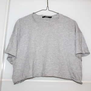 Grå croppad t-shirt från Bik Bok - Säljer en enkel och bekväm grå t-shirt från Bik Bok i storlek XL (passform som S/M). Perfekt för en avslappnad stil, med normal passform och korta ärmar. Gjord i mjukt bomullsmaterial, idealisk för vardagsbruk.