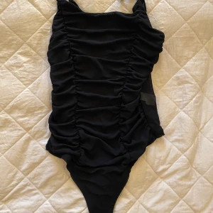 Svart body - En svart body ifrån bikbok i storlek XS. Har smala axelband som är reglerbara och små knappar nere vid botten som gör det lättare att ta av sig bodyn. Är genomskinlig på baksidan men på framsidan helt täckt och i ett lite skrunchat material. Är aldrig använd och passar mig bra i längden som är 170.