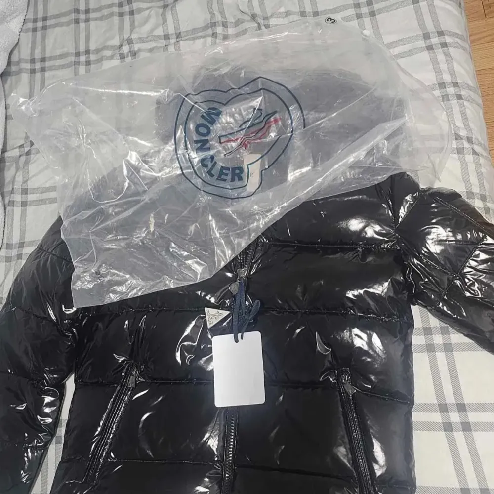 Säljer en snygg svart pufferjacka från Moncler i nytt skick. Jackan har en glansig finish och är perfekt för vintern. Den har en dragkedja framtill och en huva för extra värme. Passar perfekt för kalla dagar och håller dig varm och stilren.. Jackor.