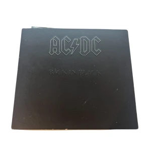 Back in Black av AC/DC - Säljer en klassisk CD av AC/DC:s album 'Back in Black'. Omslaget är stilrent svart med bandets ikoniska logga. Inuti finns bilder på bandmedlemmarna och en CD med albumets låtar. Aldrig använd, bara stått på en hylla. 