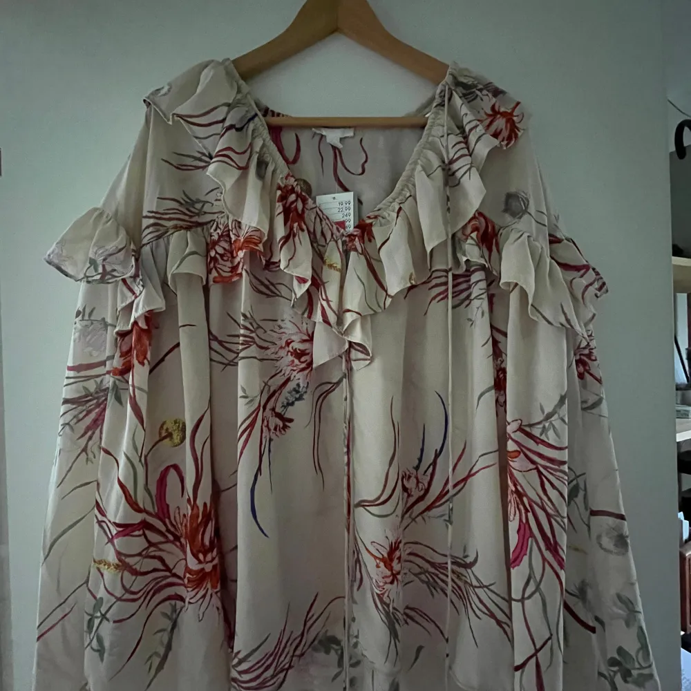 Charmig blommig klänning i ljusa färger med volangdetaljer runt halsen och ärmarna. Perfekt för sommarens fester eller en avslappnad dag i solen. Den har en lös passform som ger en luftig känsla.. Puserot.