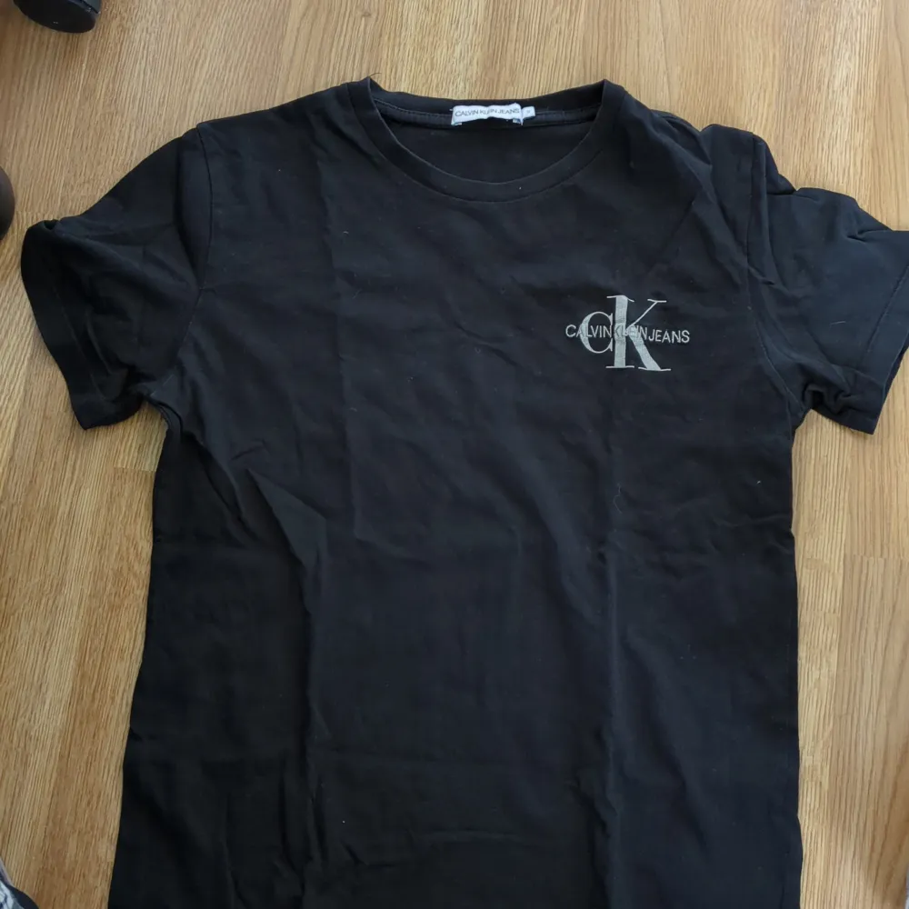 Säljer en stilren svart t-shirt från Calvin Klein Jeans. Den har en klassisk passform med korta ärmar och ett snyggt CK-logotryck på bröstet. Perfekt för en avslappnad och trendig look!. T-shirts.