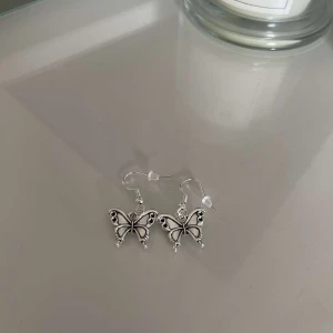 Silverfärgade fjärilsörhängen - Säljer ett par superfina silverfärgade örhängen i form av fjärilar. De har en elegant design med detaljerade vingar och små svarta accenter. Perfekta för att ge en extra touch till din outfit, oavsett om det är till vardags eller fest!
