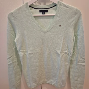 Tröja Tommy Hilfiger - Tröja från Tommy Hilfiger. Mintgrön färg. Nyskick, aldrig använd. V-ringad form. Mjuk och skön material, väldigt bekväm. Märke på höger sida. Storlek XS. 65% bomull, 35% nylon. Axelbredd 36 cm, längd 63 cm.