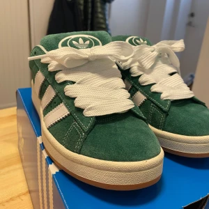 Gröna adidas campus 00 - Använda fåtal gånger så är i nyskick och har endast små oundvikliga defekter, se bilder. Skokartong samt två gröna skosnören ingår även!